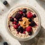 Overhead view of a jar of Protein Overnight Oats topped with fresh berries and almond butter.